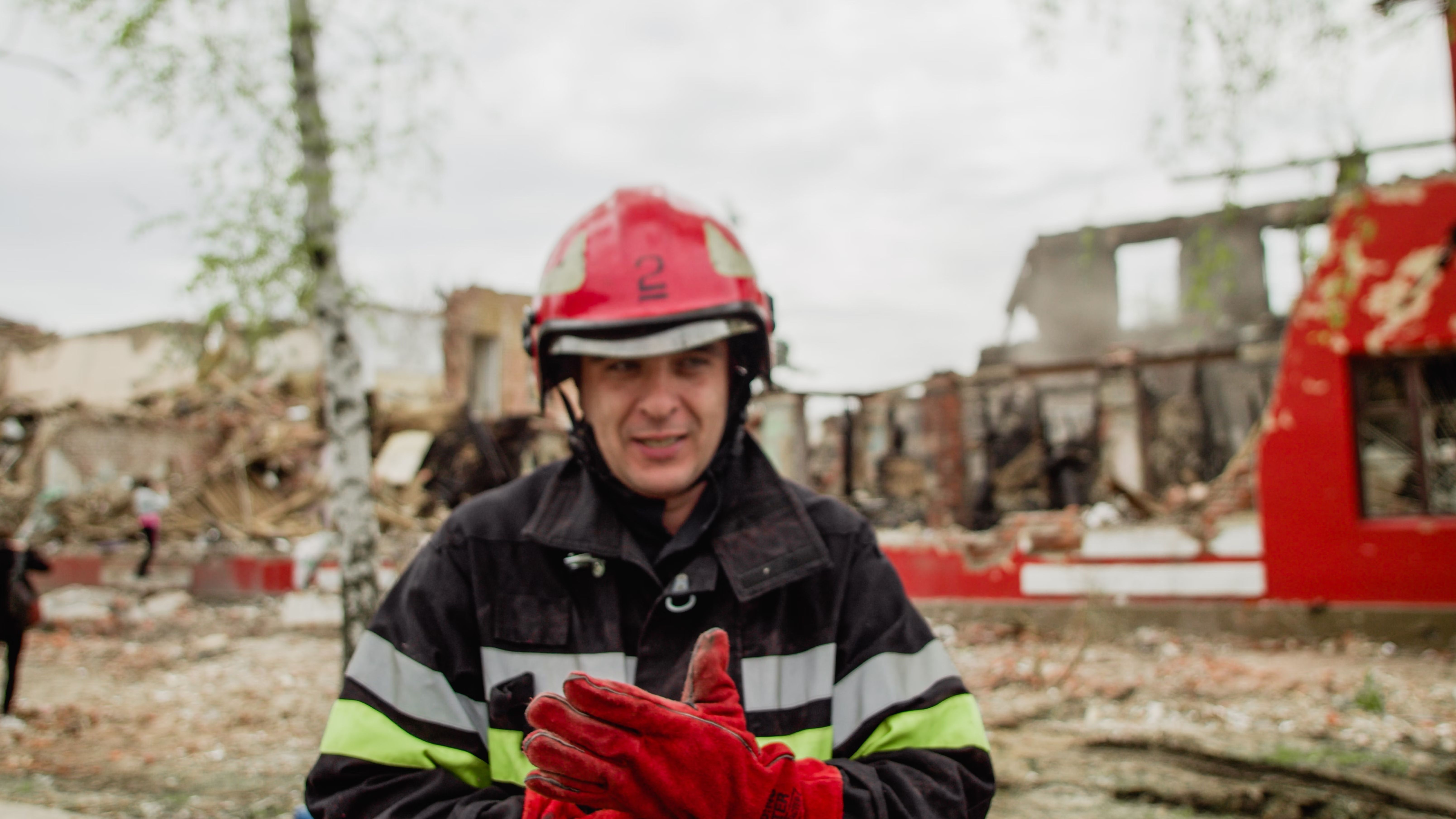 Feuerwehrmann in Schutzausrüstung und rotem Helm vor Trümmerfeld eines zerstörten Gebäudes