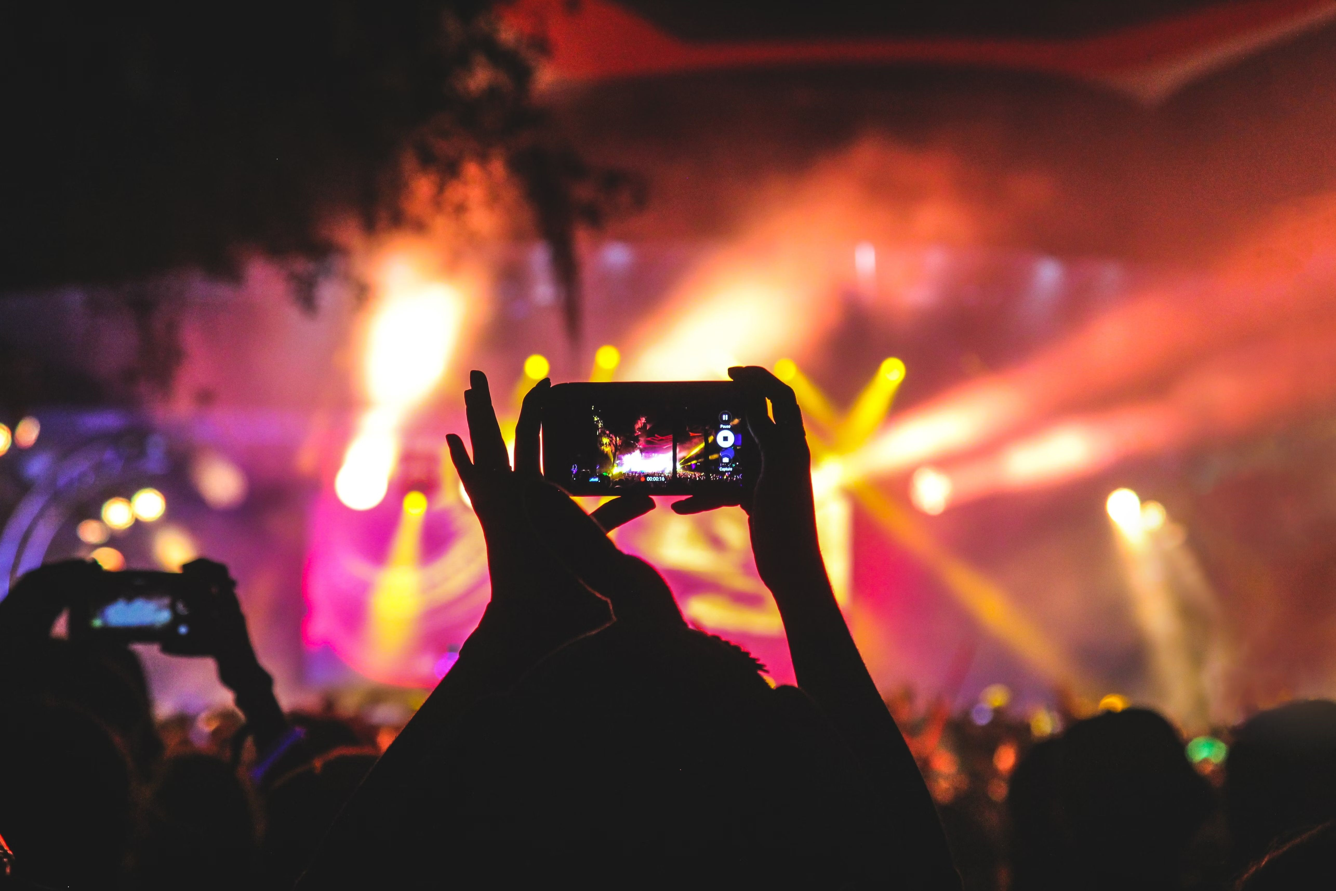 Konzertbesucher filmt mit dem Smartphone eine farbig beleuchtete Bühne bei einem Open-Air-Event